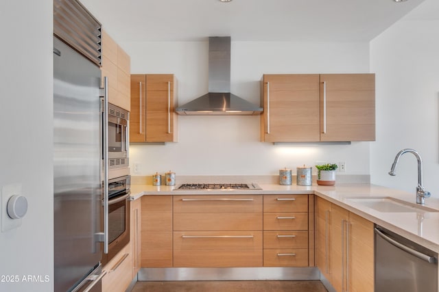 kitchen featuring stainless steel appliances, wall chimney range hood, a sink, modern cabinets, and light brown cabinets