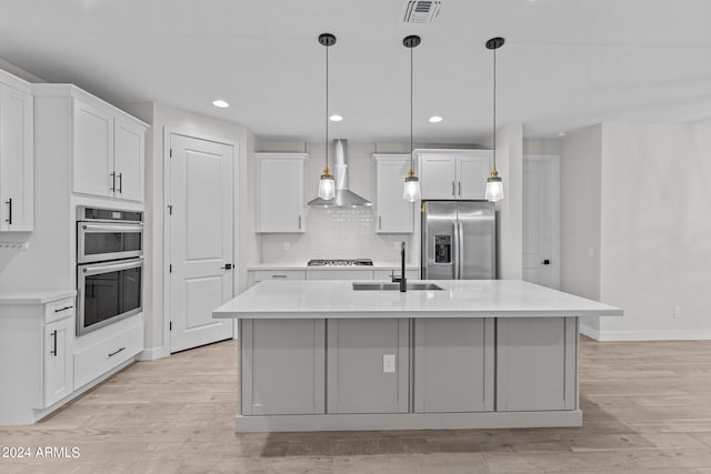 kitchen with wall chimney range hood, appliances with stainless steel finishes, sink, and white cabinetry