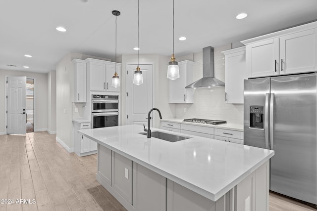 kitchen featuring white cabinets, sink, decorative light fixtures, wall chimney exhaust hood, and stainless steel appliances