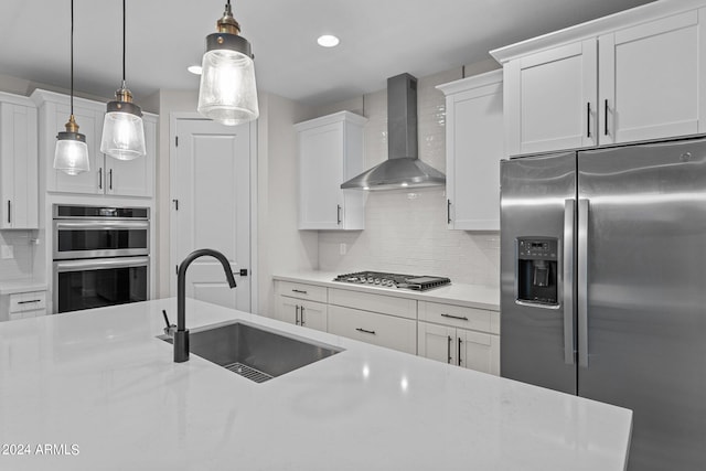 kitchen featuring pendant lighting, wall chimney range hood, appliances with stainless steel finishes, and sink