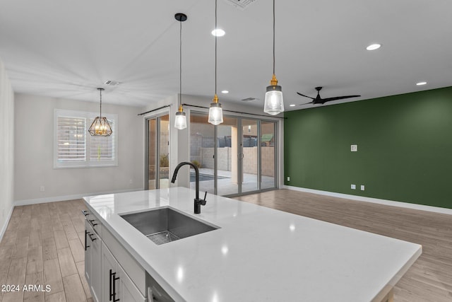 kitchen with hanging light fixtures, sink, a center island with sink, white cabinetry, and light hardwood / wood-style floors