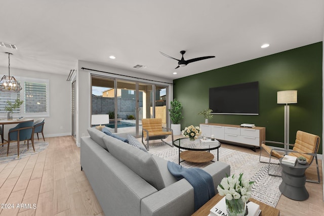 living room featuring ceiling fan with notable chandelier and light wood-type flooring