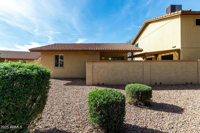 rear view of house with stucco siding, fence, a tiled roof, and central air condition unit