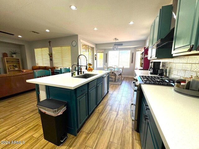 kitchen featuring sink, appliances with stainless steel finishes, a kitchen island with sink, light hardwood / wood-style flooring, and pendant lighting