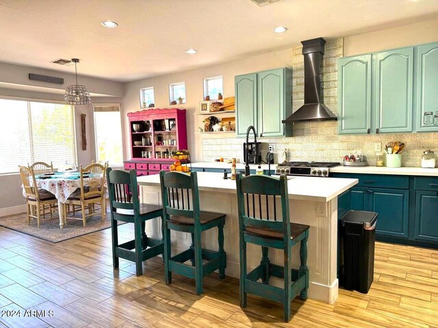 kitchen with light hardwood / wood-style floors, decorative backsplash, hanging light fixtures, stainless steel range oven, and wall chimney range hood