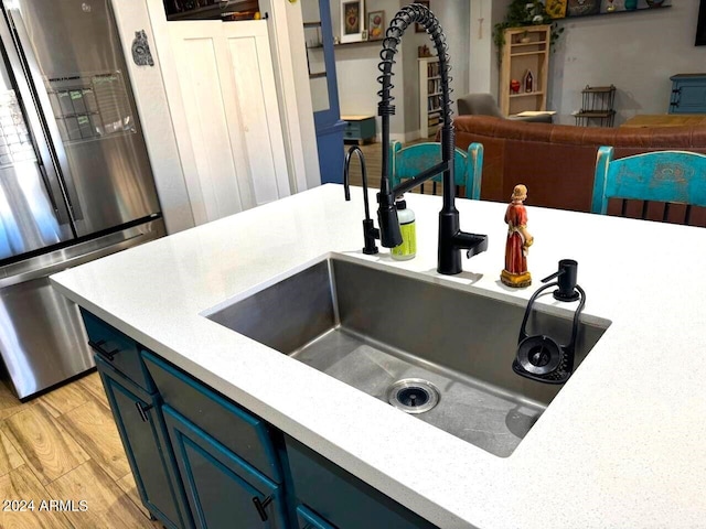 kitchen featuring blue cabinets, light wood-type flooring, sink, and stainless steel fridge