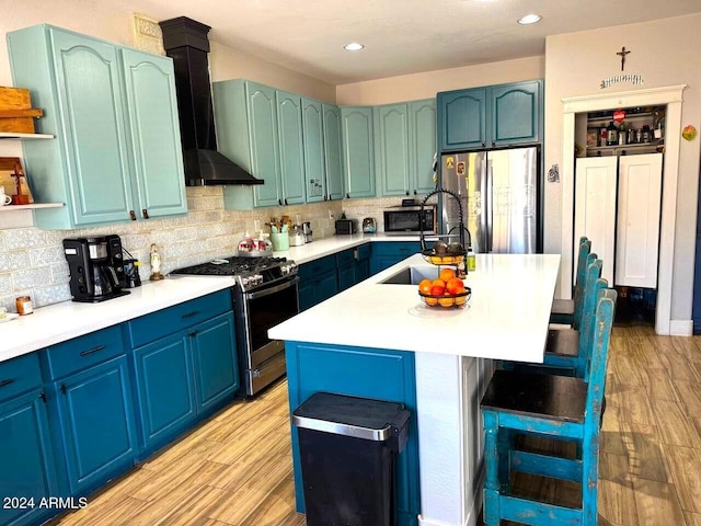 kitchen featuring a center island with sink, sink, appliances with stainless steel finishes, wall chimney range hood, and light wood-type flooring