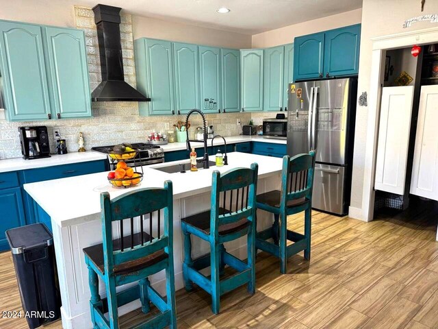 kitchen featuring stainless steel appliances, wall chimney range hood, sink, a breakfast bar, and light hardwood / wood-style floors