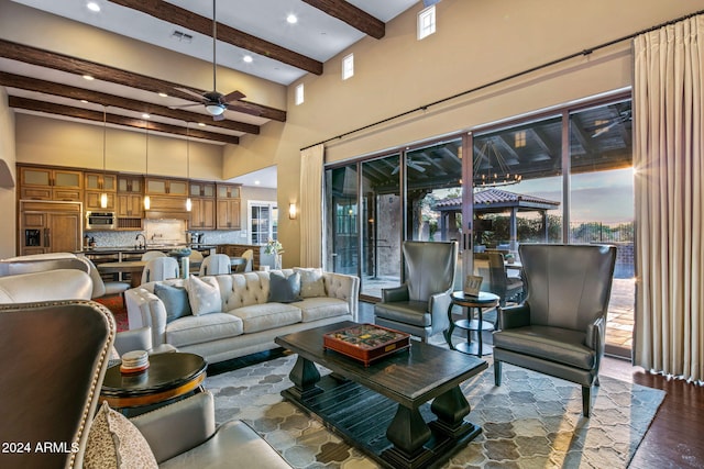 living room featuring beam ceiling, dark wood-type flooring, sink, a towering ceiling, and ceiling fan