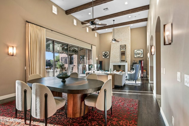 dining area featuring a large fireplace, ceiling fan, dark hardwood / wood-style flooring, beamed ceiling, and a towering ceiling