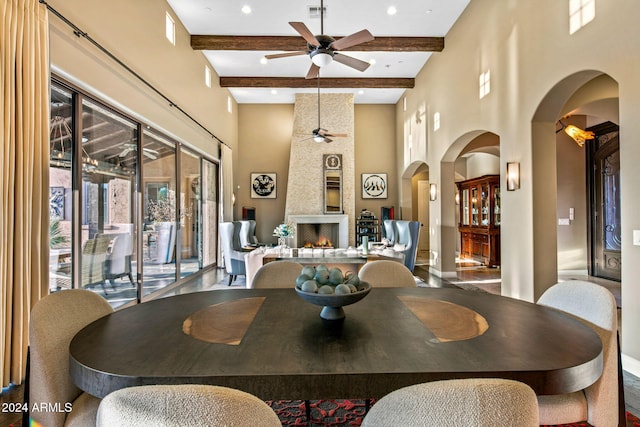 dining room with beam ceiling, a high ceiling, a large fireplace, and ceiling fan