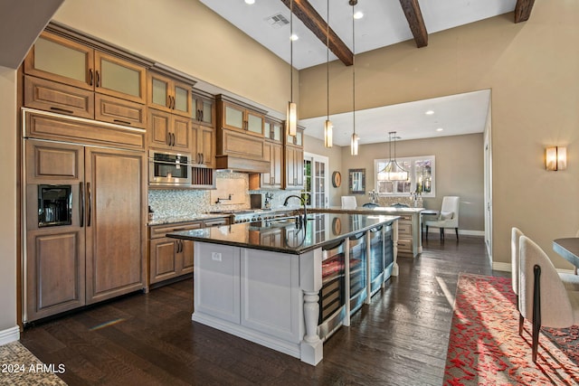 kitchen featuring dark hardwood / wood-style floors, dark stone countertops, beamed ceiling, and a center island with sink