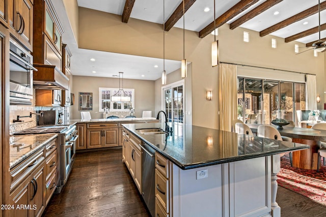 kitchen featuring a large island with sink, dark hardwood / wood-style floors, dark stone countertops, decorative light fixtures, and appliances with stainless steel finishes