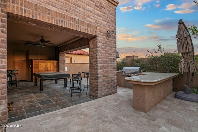 patio terrace at dusk featuring a bar, area for grilling, and ceiling fan