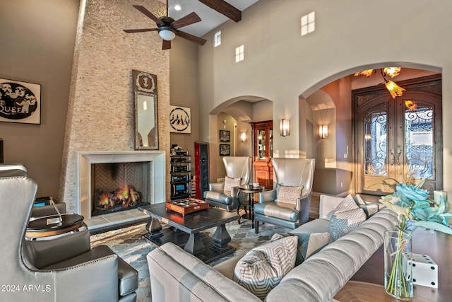 living room with a towering ceiling, beamed ceiling, a tile fireplace, and ceiling fan