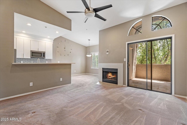 9600 N 96th St Unit 263, Scottsdale, AZ 85258 - unfurnished living room featuring light colored carpet, high vaulted ceiling, baseboards, ceiling fan, and a fireplace with flush hearth