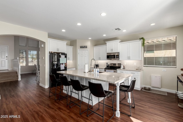 kitchen with a breakfast bar, a center island with sink, stainless steel appliances, visible vents, and white cabinetry