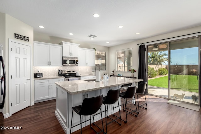 kitchen with stainless steel appliances, white cabinets, a center island with sink, and a kitchen bar