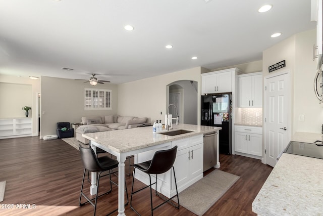 kitchen featuring a center island with sink, stainless steel dishwasher, white cabinetry, a sink, and a kitchen bar