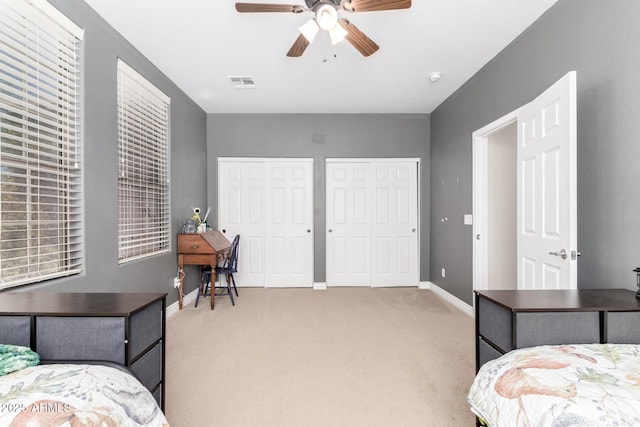 bedroom with multiple closets, visible vents, light carpet, ceiling fan, and baseboards