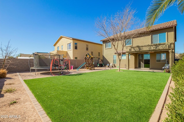 rear view of house with a fenced backyard, a trampoline, a yard, a playground, and stucco siding