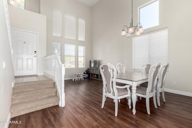 dining room featuring a notable chandelier, a towering ceiling, dark wood-type flooring, baseboards, and stairs