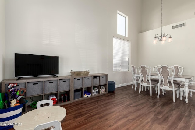 dining room featuring wood finished floors, visible vents, a towering ceiling, and an inviting chandelier