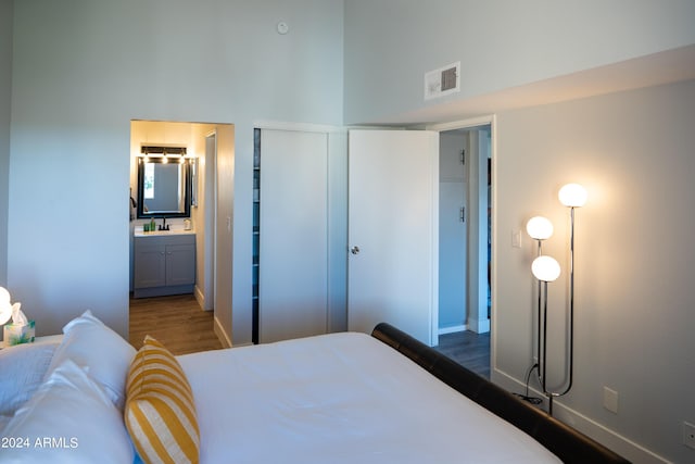 bedroom with dark wood-type flooring, a high ceiling, sink, ensuite bath, and a closet