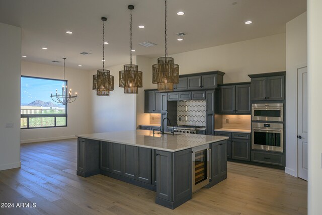 kitchen featuring a large island with sink, stainless steel double oven, pendant lighting, beverage cooler, and light hardwood / wood-style flooring