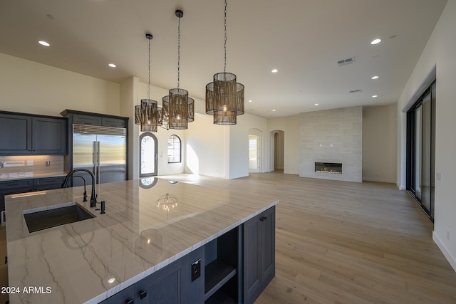 kitchen featuring sink, light wood-type flooring, light stone counters, a fireplace, and stainless steel built in refrigerator