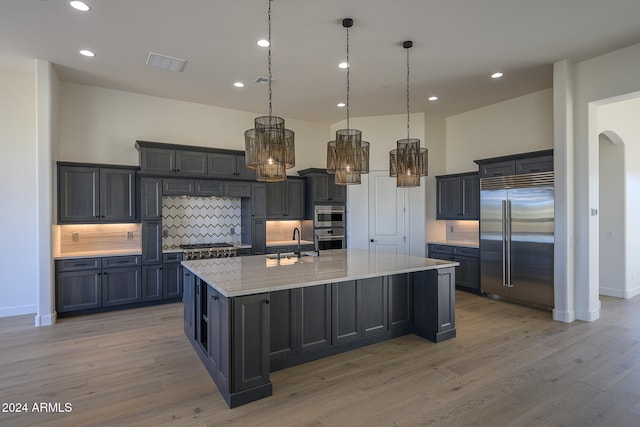 kitchen featuring a large island, light stone counters, stainless steel appliances, light hardwood / wood-style floors, and decorative light fixtures