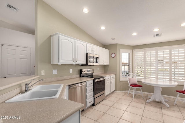 kitchen featuring light tile patterned flooring, lofted ceiling, sink, white cabinetry, and stainless steel appliances