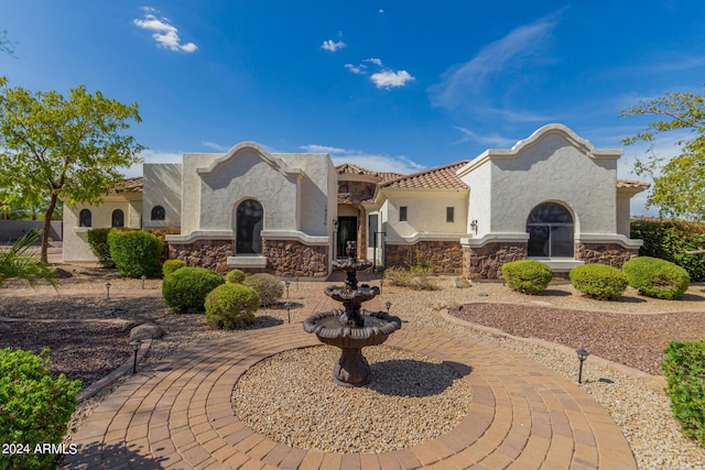 mediterranean / spanish house with a tile roof, stone siding, and stucco siding