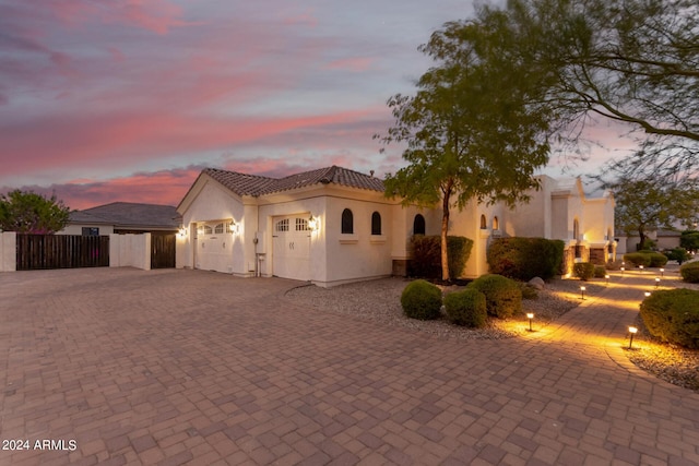 mediterranean / spanish-style home with stucco siding, decorative driveway, fence, and a garage