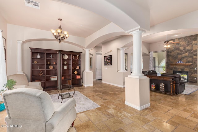 foyer featuring a stone fireplace, visible vents, ceiling fan with notable chandelier, ornate columns, and stone tile floors