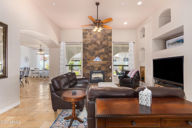living room with stone tile flooring, a fireplace, baseboards, ceiling fan, and arched walkways