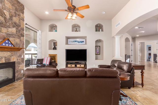 living room featuring ceiling fan, visible vents, arched walkways, a fireplace, and stone tile floors