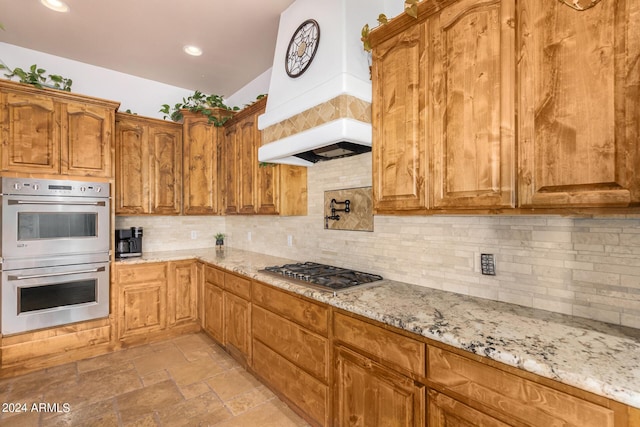 kitchen with appliances with stainless steel finishes, brown cabinetry, light stone counters, and tasteful backsplash