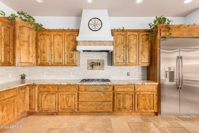 kitchen with custom range hood, stone tile floors, light stone counters, and stainless steel appliances