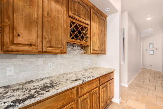 bar featuring visible vents, a dry bar, tasteful backsplash, baseboards, and stone tile flooring