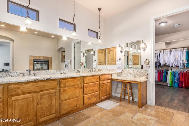 bathroom with visible vents, stone tile flooring, a towering ceiling, a tile fireplace, and a sink