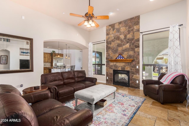 living area featuring arched walkways, ceiling fan, a fireplace, and stone tile floors