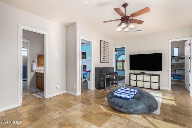 living room with stone tile floors, a ceiling fan, baseboards, and visible vents