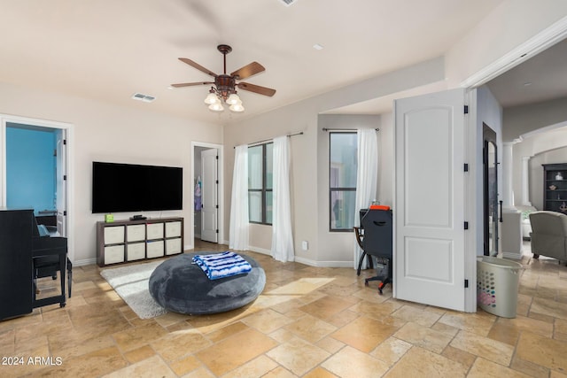 living room with ceiling fan, visible vents, baseboards, and stone tile flooring