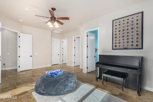 sitting room with baseboards, visible vents, a ceiling fan, and stone tile floors