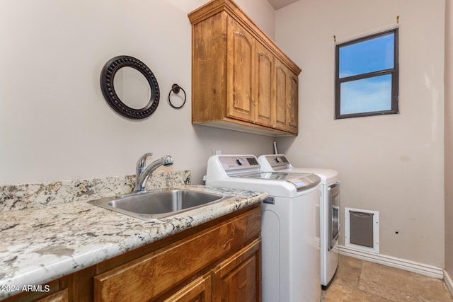 washroom with cabinet space, a sink, baseboards, stone finish flooring, and washer and clothes dryer