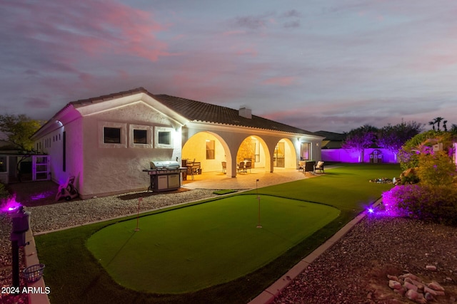 back of property at dusk with a chimney, a tile roof, a patio area, and stucco siding