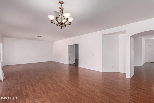 spare room with arched walkways, dark wood finished floors, and a notable chandelier