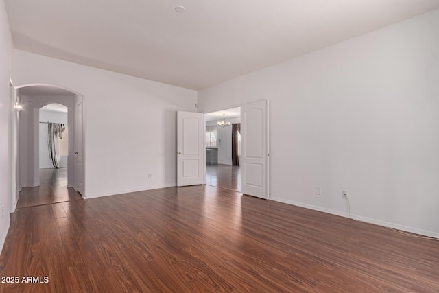 empty room featuring dark wood-style flooring, arched walkways, and baseboards