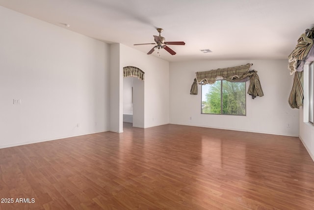 empty room featuring ceiling fan, arched walkways, baseboards, wood finished floors, and visible vents